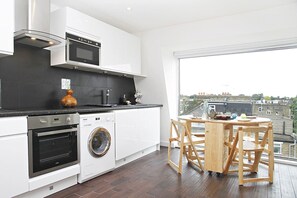 A modern kitchen with a washing machine, oven, and microwave. There is a dining area with a table and chairs. - Penthouse with balcondy and Panoramic Views (Greater London)