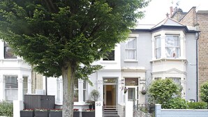 Uma casa geminada de dois andares com porta de entrada, o número '95' visível e uma árvore em primeiro plano.