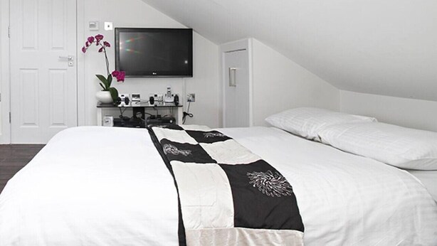 Quarto moderno com uma cama grande, televisão de tela plana e escrivaninha com computador e outros objetos.