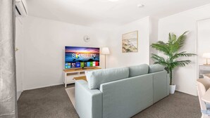 En stue med en grå sofa, et fladskærms-TV, en plante og et vægur.