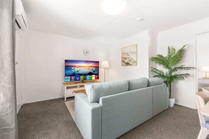 A living room with a grey sofa, a flat-screen TV, a plant, and a wall clock. - Peaceful 1-Bed Apartment in Kedron with Parking (Kedron)