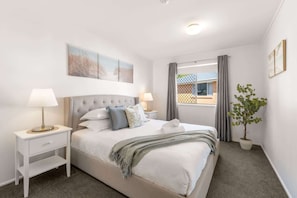 A bedroom with a bed, two bedside tables, a window with curtains, a plant, and artwork on the wall. - Peaceful 1-Bed Apartment in Kedron with Parking (Kedron)