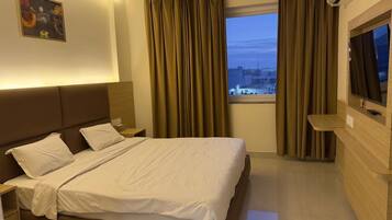 Una habitación de hotel con cama, televisión, mesita de noche, ventana con cortinas y vista a la ciudad.