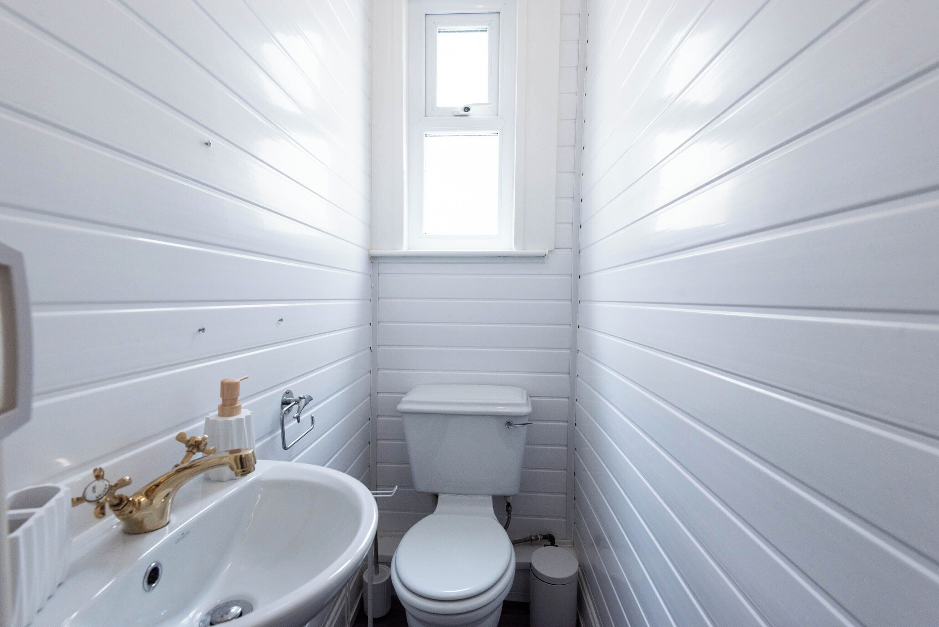 A small, white bathroom with a sink, toilet, and window.
