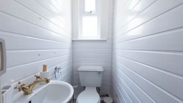 A small, white bathroom with a sink, toilet, and window.