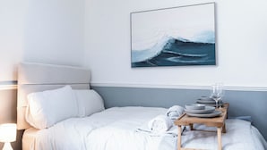 A neatly made bed with white linens, a bedside table with a lamp, and a tray with plates and glasses. - The Bay Apart-Hotel by Guestz (Morecambe)