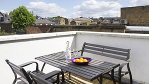 Terraço no telhado com mesa e cadeiras, uma tigela de frutas e uma garrafa de champanhe.