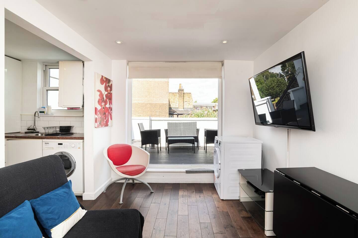 Un espacio habitable compacto con kitchenette, televisor de pantalla plana, zona de estar con una silla roja y vistas a un balcón exterior.