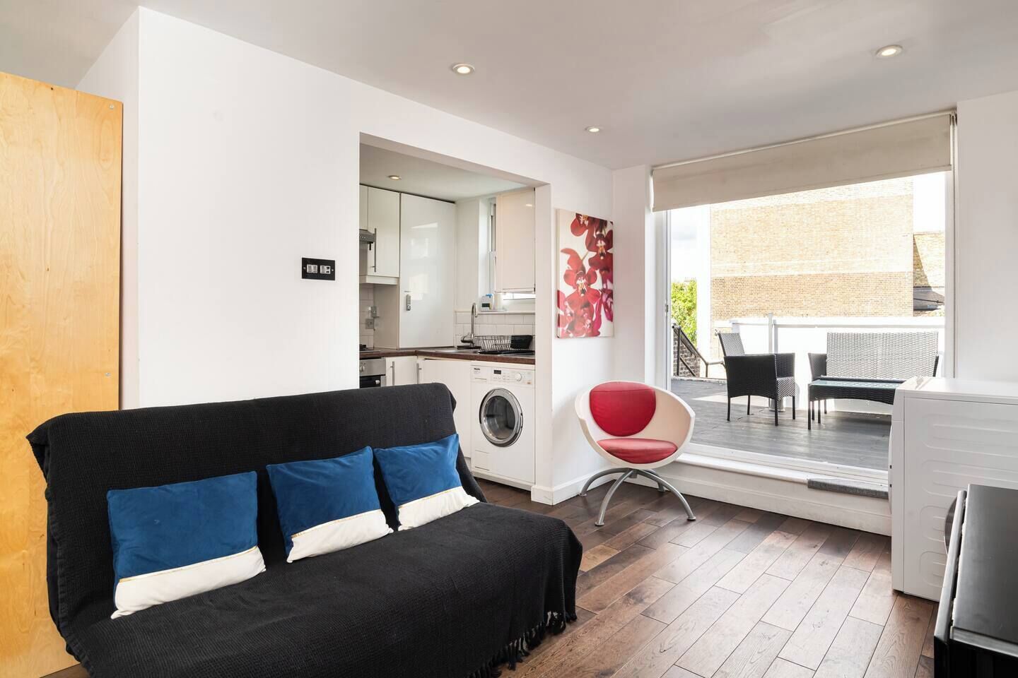 Ein zeitgemäßer Wohnraum mit Sofa, einem roten Sessel, einer Waschmaschine und einem Essbereich mit Aussicht.