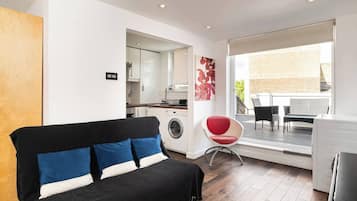 Un espace de vie moderne comprenant un canapé, un fauteuil rouge, un lave-linge et un coin repas avec vue.