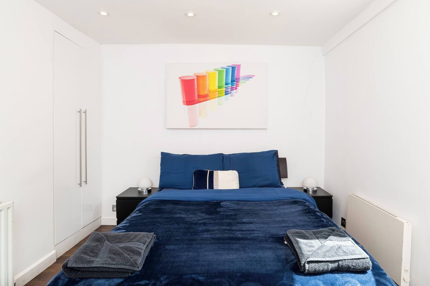 Ein Schlafzimmer mit einem Bett, zwei Nachttischen, einem Wandbild und einer Heizung.