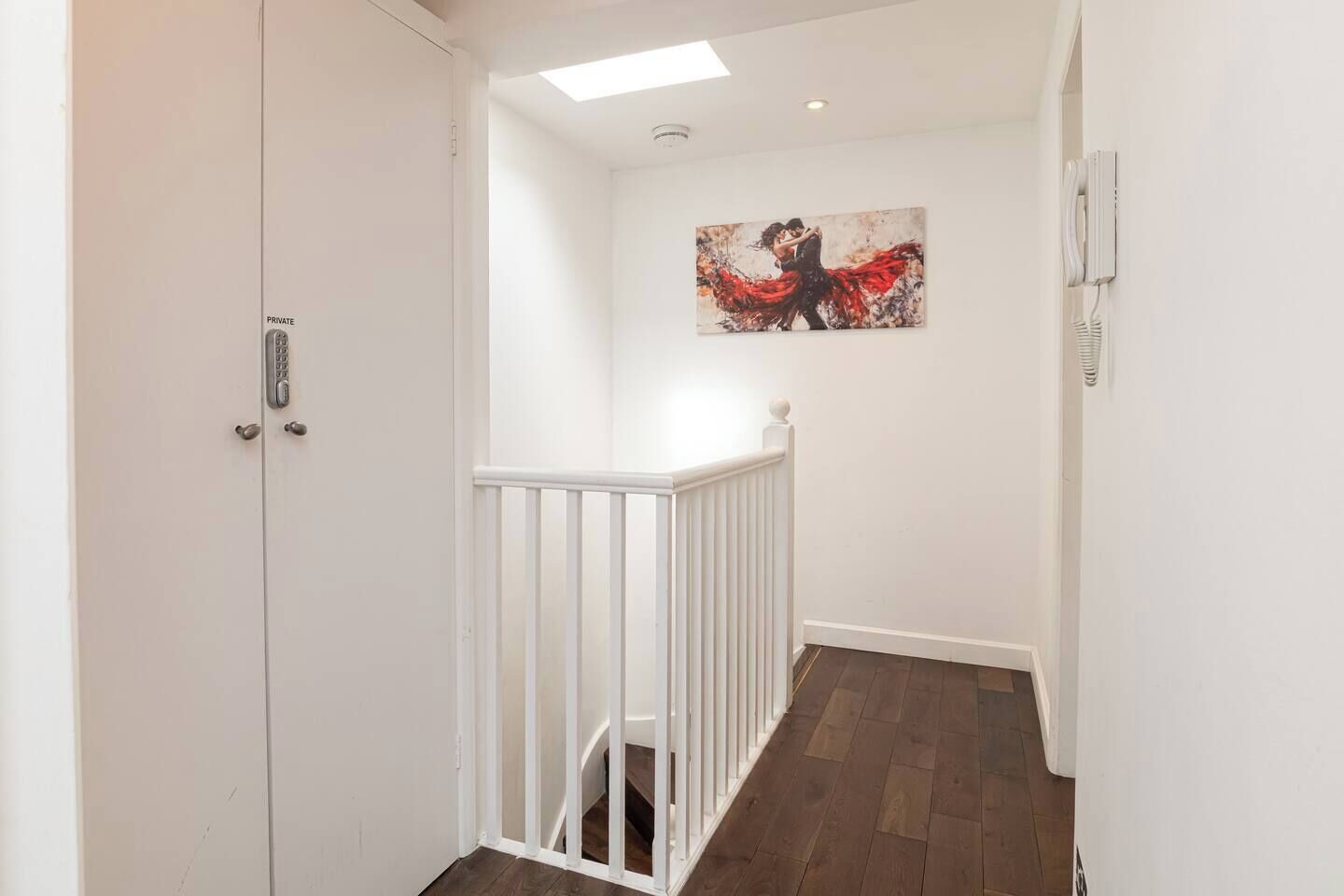A hallway with a white door, a white railing, and a painting on the wall.