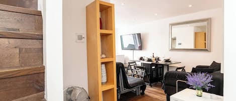 Un salon moderne avec une bibliothèque en bois, un coin repas équipé d’un téléviseur et un canapé agrémenté d’un vase de fleurs.