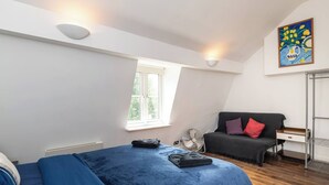 Quarto com cama, escrivaninha, cadeira, radiador, janela e um quadro na parede.