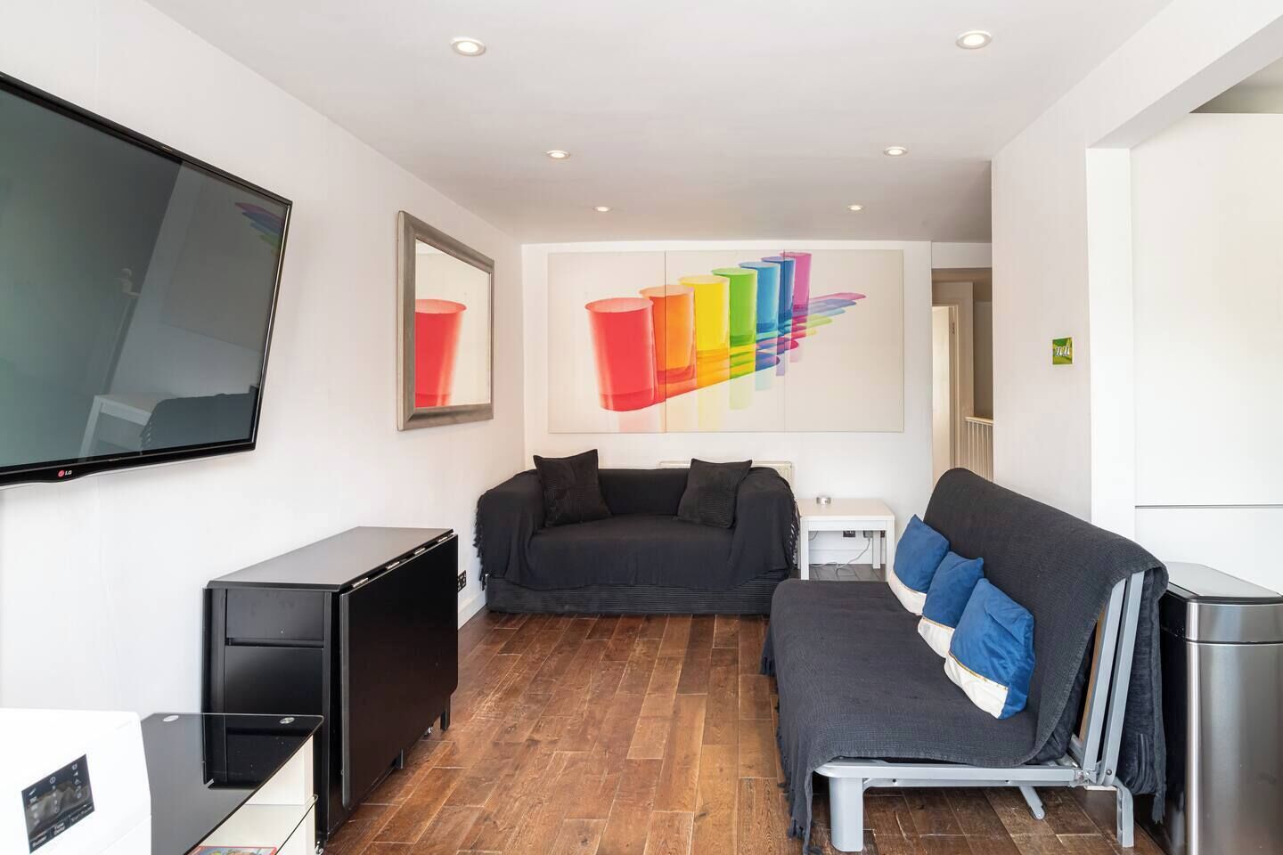 Ein modernes Wohnzimmer mit einem Flachbildfernseher, einer Couch, einem Couchtisch und einem farbenfrohen, abstrakten Gemälde an der Wand.