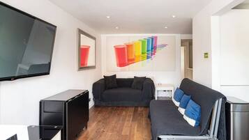 Ein modernes Wohnzimmer mit einem Flachbildfernseher, einer Couch, einem Couchtisch und einem farbenfrohen, abstrakten Gemälde an der Wand.