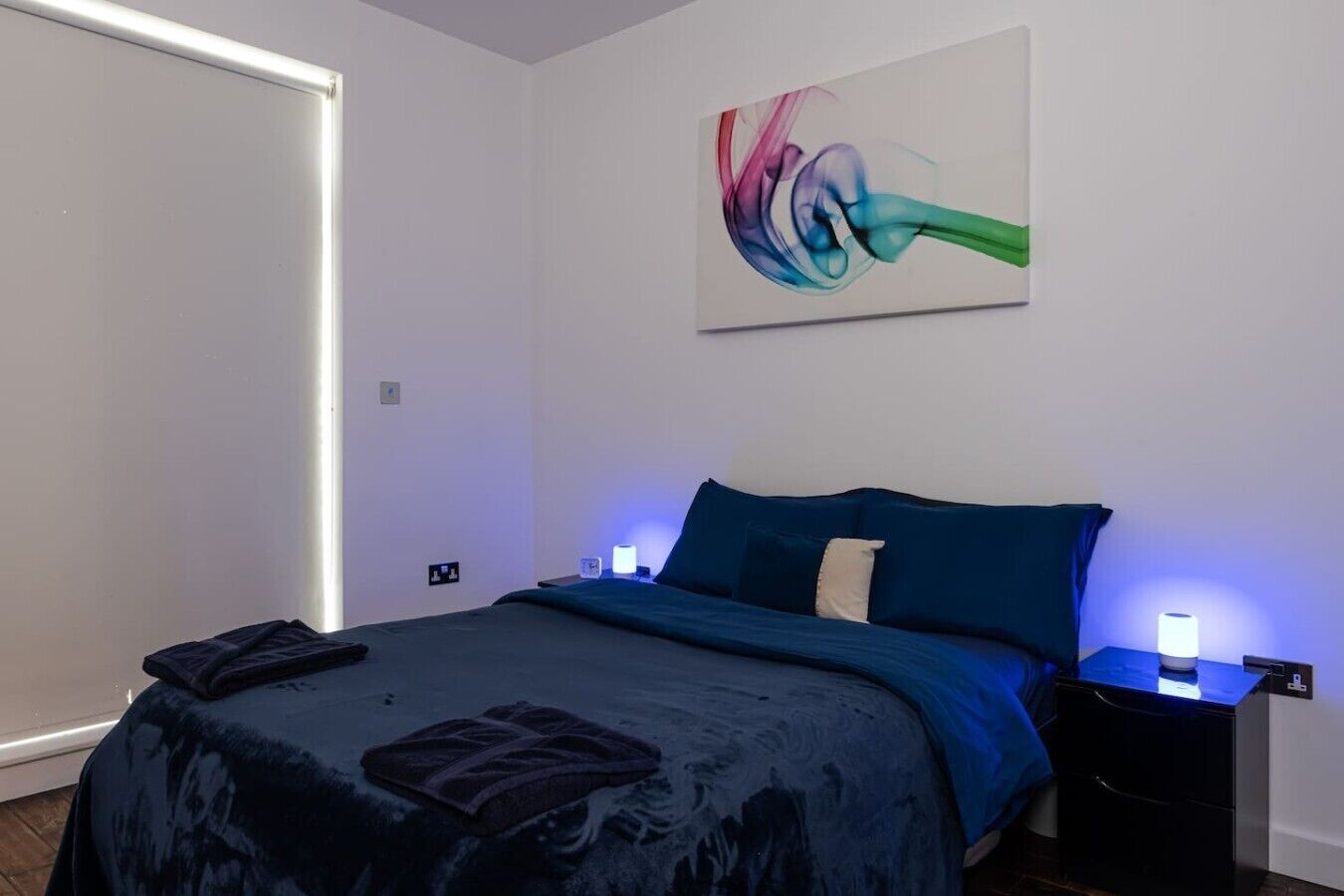 Ein Schlafzimmer mit einem Bett, einem an der Wand hängenden abstrakten Gemälde und Nachttischlampen.