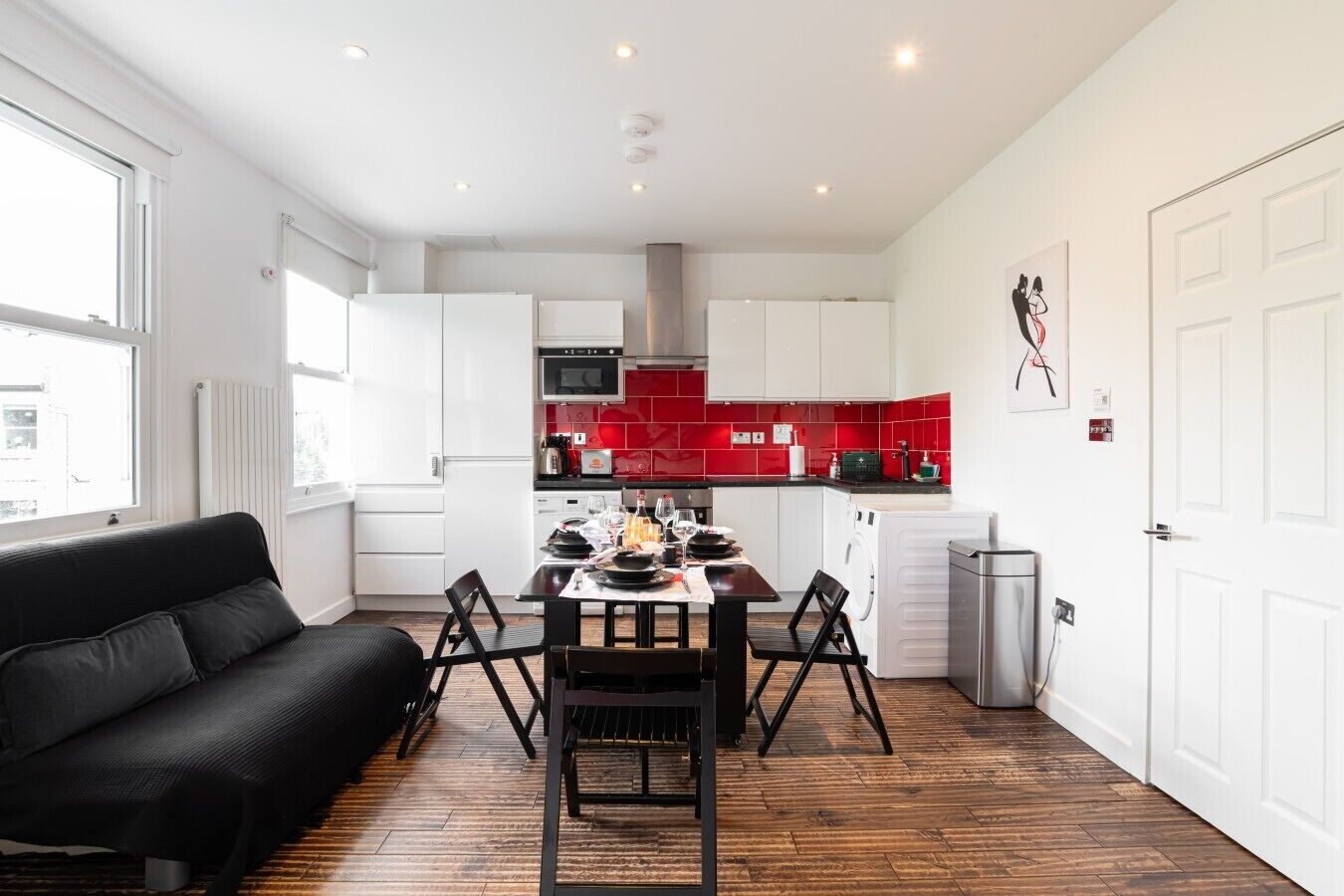 A modern kitchen with white cabinets, a red backsplash, and a dining area with a black table and chairs.