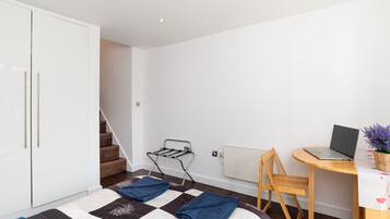 Une chambre à coucher avec un lit, un bureau avec un ordinateur portable, un radiateur et un escalier.