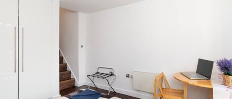 A bedroom with a bed, a desk with a laptop, a radiator, and a staircase.