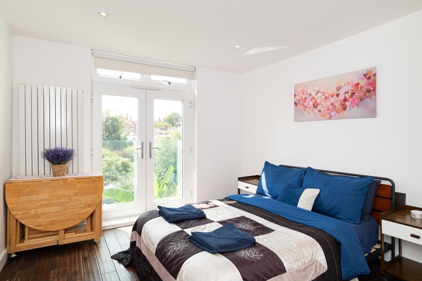 Ein Schlafzimmer mit einem Bett, einem Holztisch und einem Fenster mit Blick auf Grünflächen.