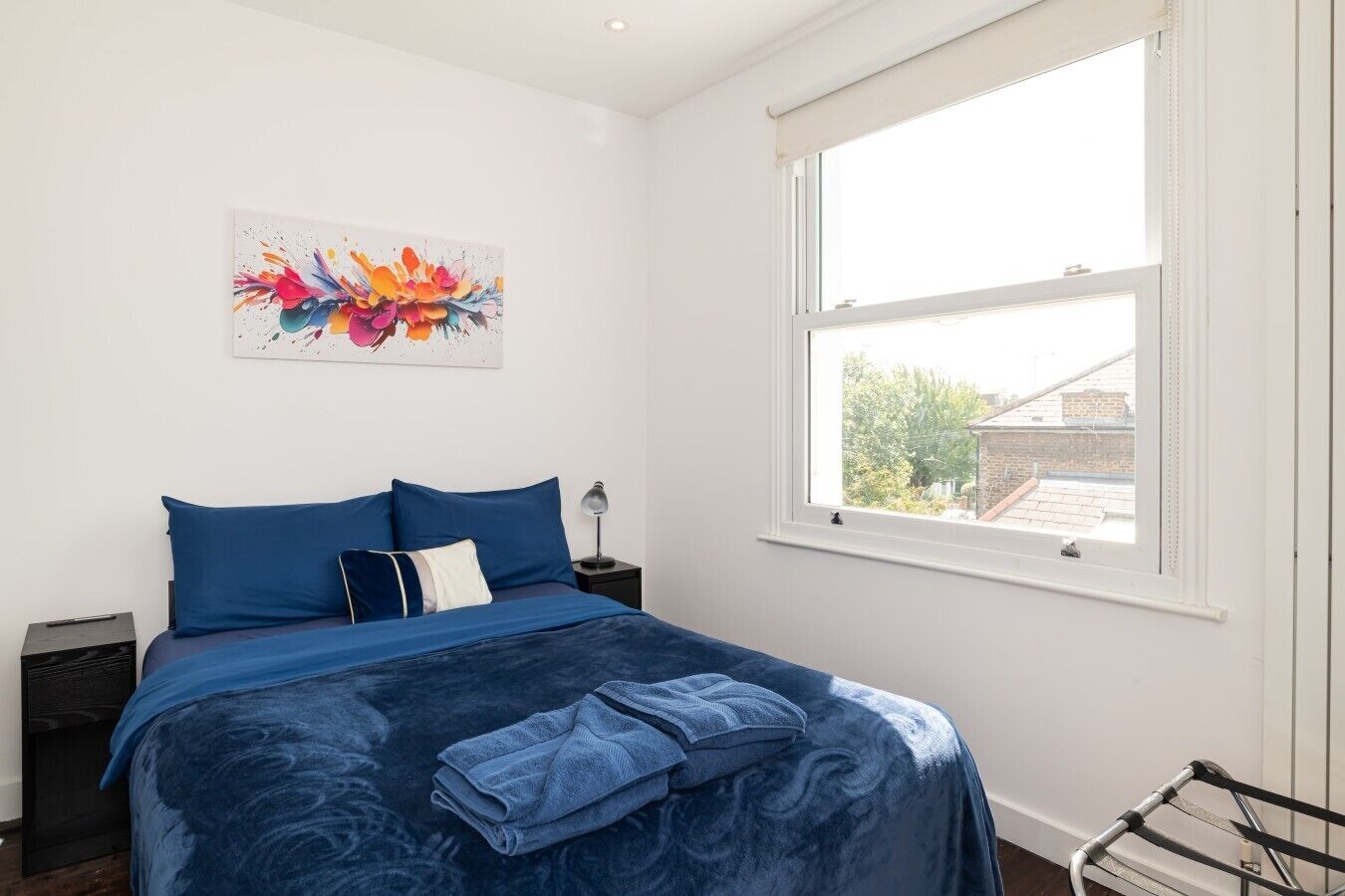A bedroom with a bed, a window, a nightstand, and a wall art piece.
