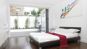 Ein modernes Schlafzimmer mit einem großen Bett, Blick auf einen Garten und einer Schiebeglastür.