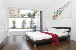 A modern bedroom with a large bed, a view of a garden, and a sliding glass door. - 2BR Family Garden Flat Sleeps 8 (Greater London)