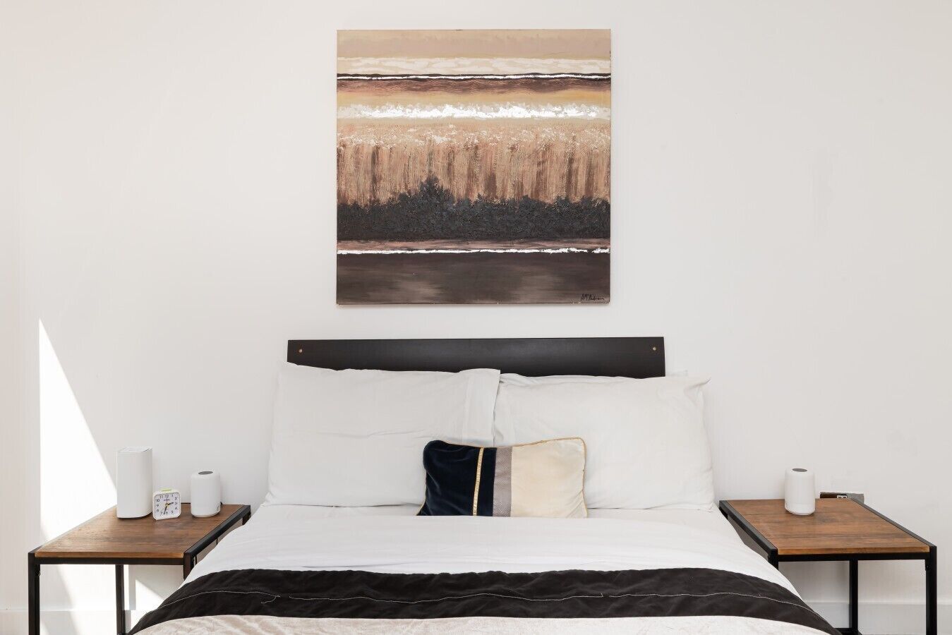 Ein Schlafzimmer mit einem Bett, zwei Nachttischen, einem Wandbild und einem Fenster, das einen Schatten wirft.