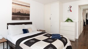 Una camera d'albergo con un letto, un comodino, una cassettiera, un quadro e una porta che dà su un'altra stanza.