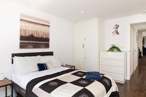A hotel room with a bed, a nightstand, a dresser, a painting, and a door leading to another room. - 2BR Family Garden Flat Sleeps 8 (Greater London)