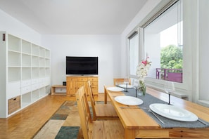 A modern kitchen with white cabinetry, a dining table set for four, and a large window with a view of greenery. - Spacious Apartment for Friends | Balcony & Workspace (Wrocław)