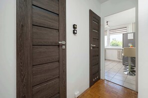 A hallway with wooden doors, a light switch, and a window with blinds. - Spacious Apartment for Friends | Balcony & Workspace (Wrocław)