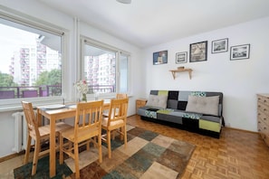 A living room with a dining table, chairs, a sofa, and a view of buildings through a window. - Spacious Apartment for Friends | Balcony & Workspace (Wrocław)
