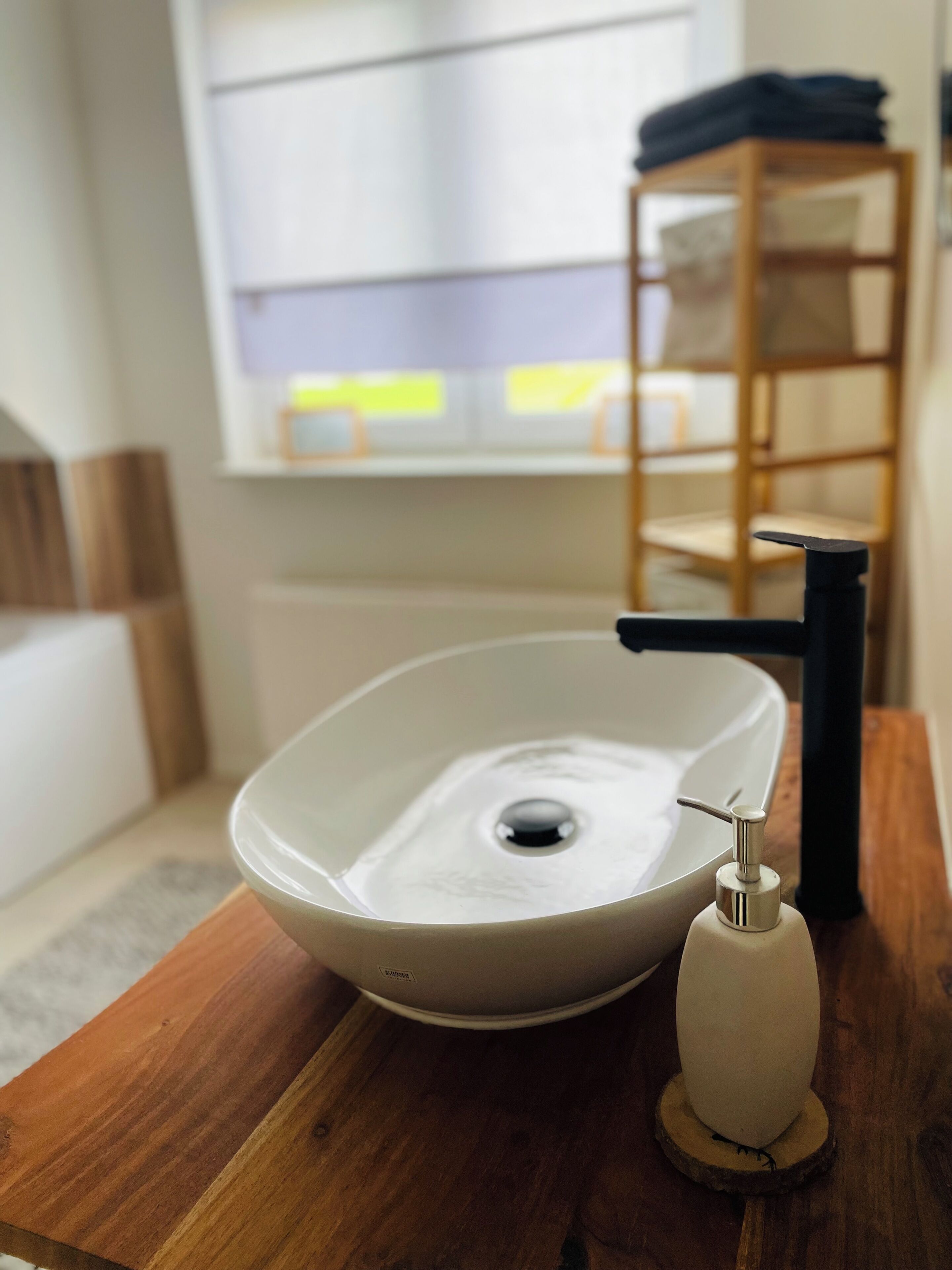 A bathroom with a white sink, a black faucet, and a wooden shelf in the background.