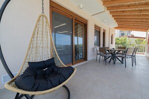 Ein Hängesessel mit Moskitonetz, ein Esstisch mit Stühlen und eine Glasschiebetür, die auf einen Balkon führt.