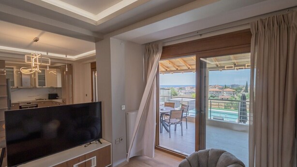 En moderne stue med et fladskærms-tv, et spiseområde med et bord og stole, og en balkon med havudsigt.