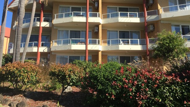 A multi-story building with balconies, brick exterior, and surrounding vegetation.