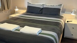 A neatly made bed with striped bedding, two pillows, a bedside lamp, and a nightstand with a remote control.