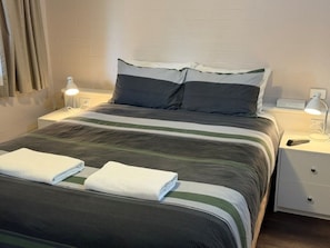 A neatly made bed with striped bedding, two pillows, a bedside lamp, and a nightstand with a remote control.