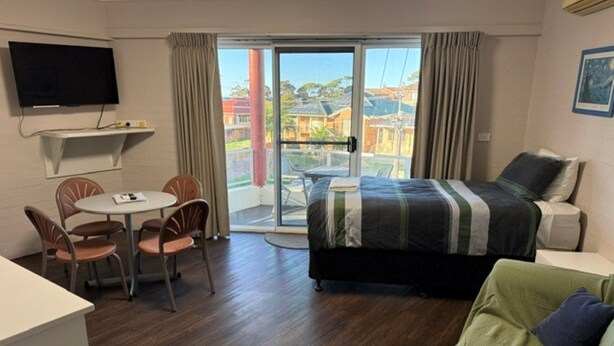 Een hotelkamer met een bed, een bureau met stoelen, een televisie en een balkon met gordijnen.