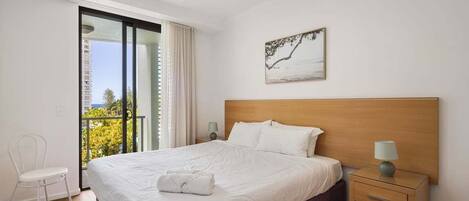 A hotel room with a bed, a nightstand, a chair, a painting, and a balcony with a view.