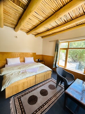 Una habitación con una cama de madera, una mesa y un ventanal con vistas a zonas verdes.