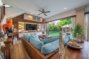 Ein modernes Wohnzimmer mit großem Fernseher, Holzmöbeln und Blick auf einen Garten.