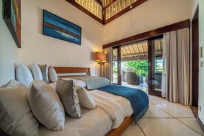 Ein Schlafzimmer mit einem großen Bett, einem Nachttisch, einer Lampe und Blick ins Freie durch eine Schiebetür.