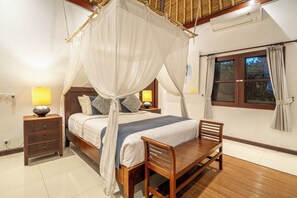 A bedroom with a four-poster bed, bedside lamps, a wooden nightstand, a wooden chair, and a window with curtains.