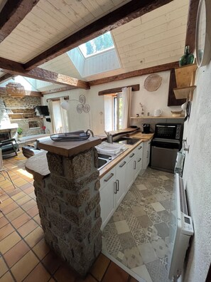 A kitchen with a stone island, wooden beams, a skylight, a flat-screen TV, and a built-in oven. - Charming house * Penty Breton * private spa * enclosed garden * beaches within walking distance (Lampaul-Plouarzel)