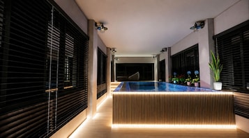 A modern indoor pool area with a central pool, wooden paneling, and potted plants.