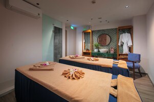 Habitación de spa con dos camillas de masaje, toallas, una bata, un lavabo y un espejo.