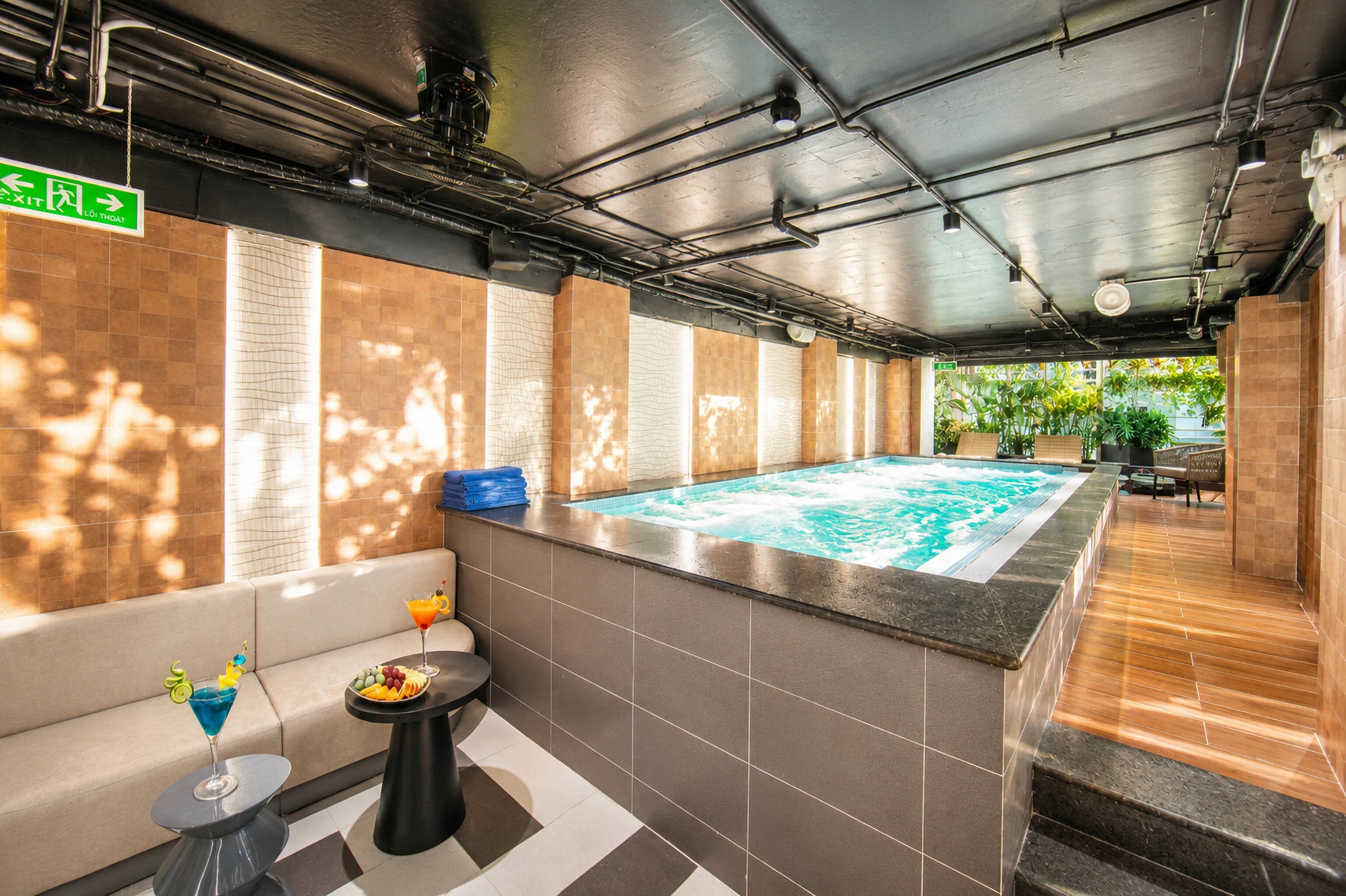 Un área de spa con un jacuzzi, una pequeña mesa con bebidas y fruta, y una piscina.